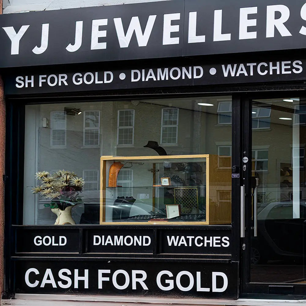 YJ Jewellers storefront with glass window displaying jewellery and signs advertising gold, diamond, and watch services.